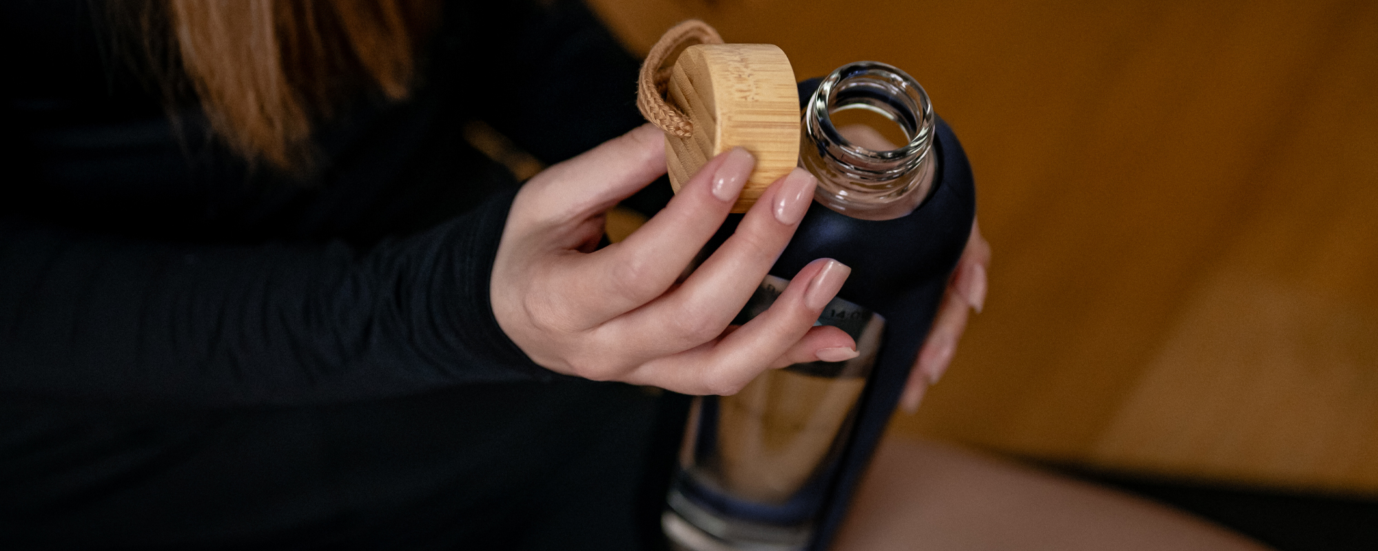 Odkręcona butelka szklana KiCA Hydro Glass 1000 ml - granatowa trzymana w dłoniach przez kobietę