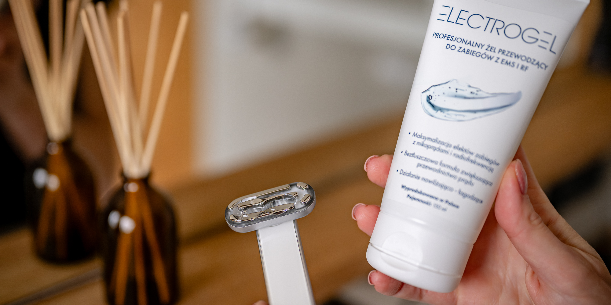 Żel przewodzący Humanas Electrogel trzymany w dłoni przez kobietę. W drugiej ręce trzyma urządzenie wykorzystujące technologie EMS i RF