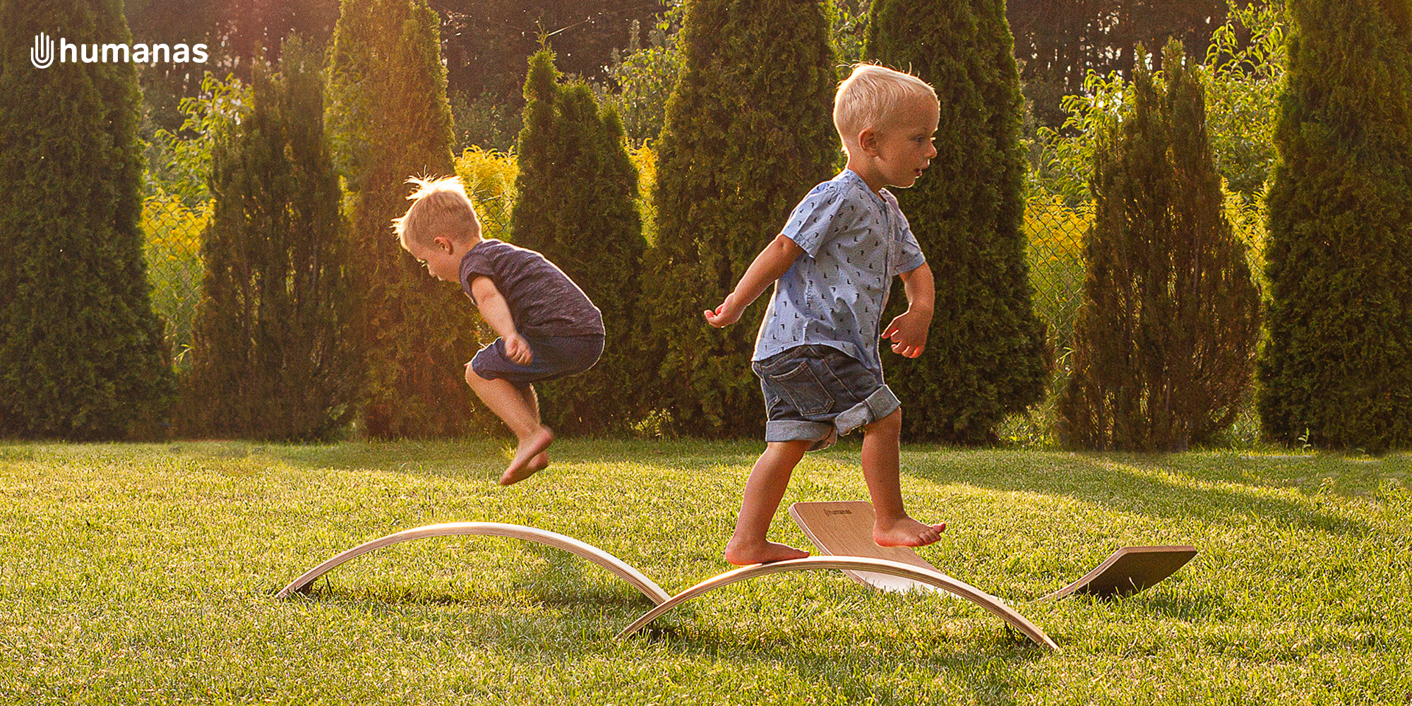 Dwóch małych chłopców bawi się deską do balansowania Humanas BoardOne w ogrodzie