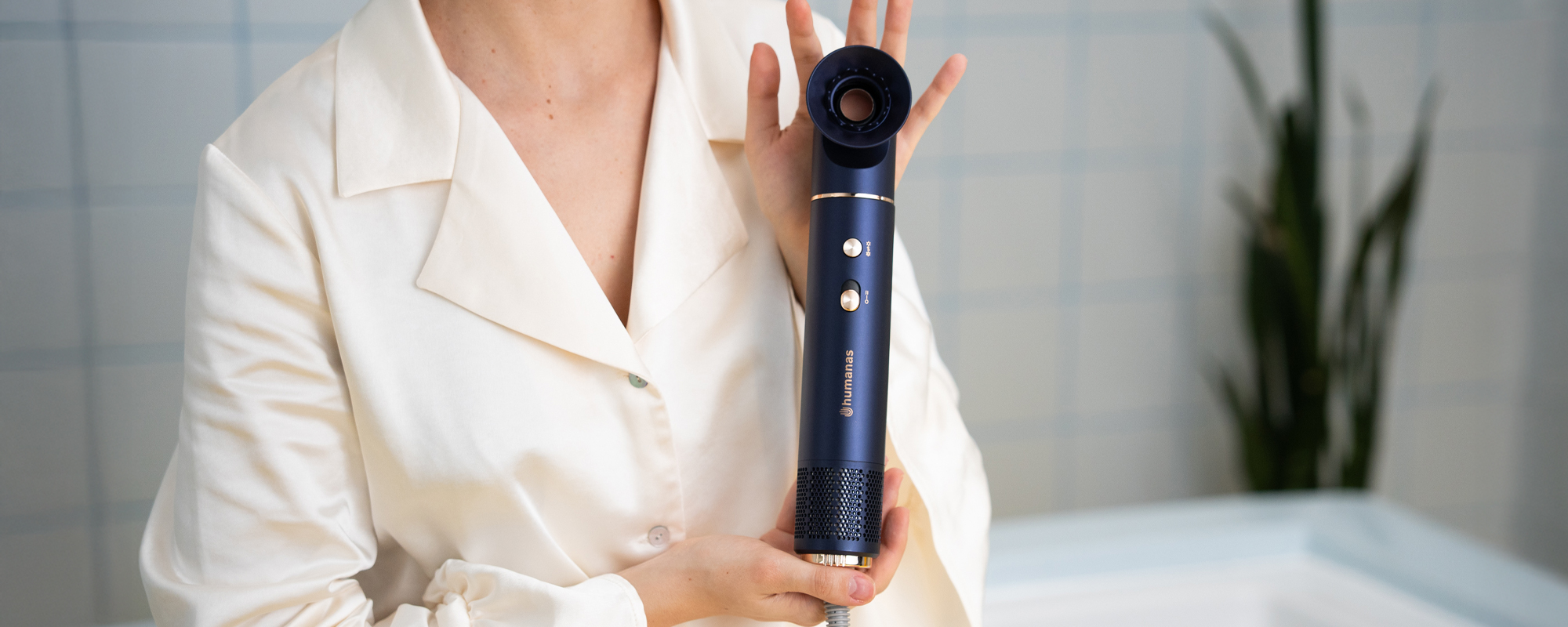 Kobieta trzymająca w dłoniach suszarkę do włosów z funkcją jonizowania Humanas AirTouch HD-AT05. W tle kafelki oraz wanna.