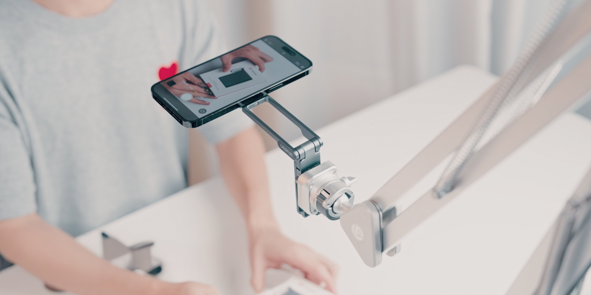 width=100% Uchwyt do smartfona Ulanzi MA38 na ramieniu ustawiony nad biurkiem ze smartfonem